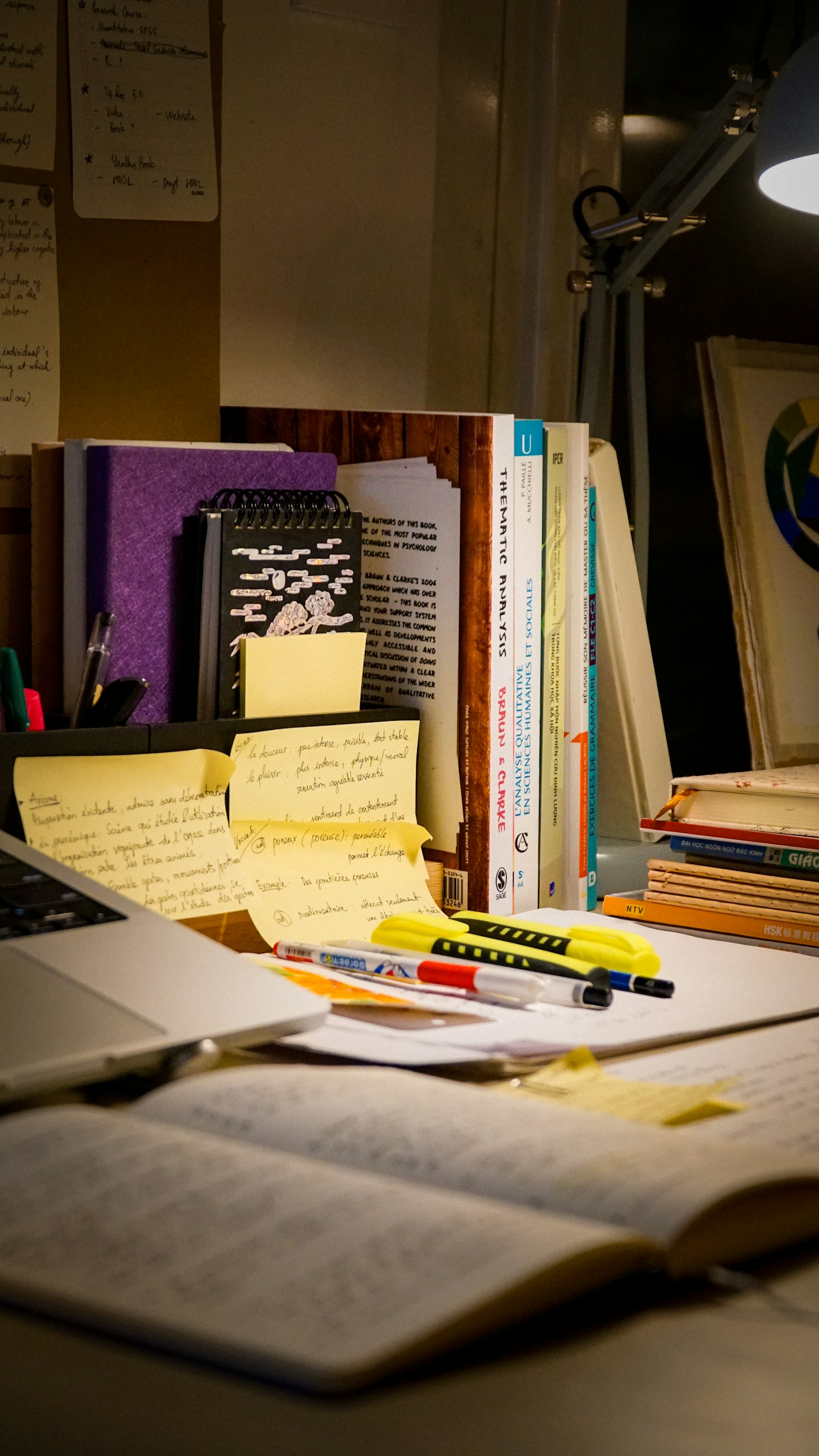 A desk with a laptop, open books, handwritten notes, and study materials