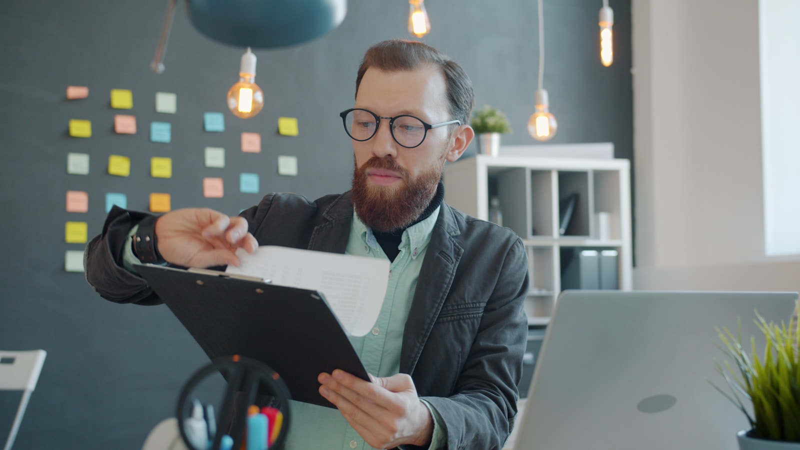 A man in glasses comparing printed documents beside a laptop